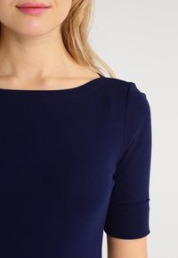 Marinblå, figursydd topp med bred båturringning och korta, uppvikta ärmar. Slät, elastisk tyg och rena sömnadsdetaljer.