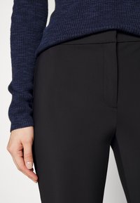 Pantalon noir sur mesure en tissu lisse, avec une poche latérale discrète. Accompagné d'un pull côtelé marine.