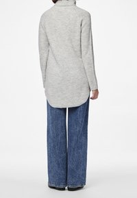 Jasnoszary sweter z dzianiny z wysokim kołnierzem, długimi rękawami oraz dłuższym tylnym brzegiem. Połączony z szerokimi dżinsami i czarnym obuwiem.
