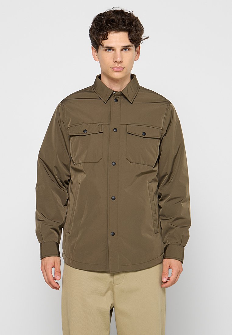Veste légère vert olive avec fermeture à pression, deux poches poitrine et manches longues. Tissu lisse et légèrement brillant, design décontracté.