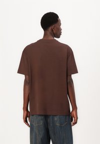 Braunes Baumwoll-T-Shirt mit kurzen Ärmeln, rundem Halsausschnitt, lässiger Passform und flachen Nähten, kombiniert mit blauen Jeans.