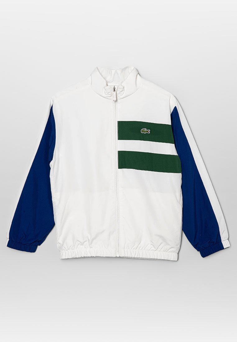 Veste zippée blanche avec des manches bleues, des rayures horizontales vertes et blanches sur le devant, et un petit logo vert sur la poitrine.