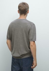 Grå kortærmet skjorte med rund halsudskæring, lavet af et letvægtsstof, der har en glat tekstur og en afslappet pasform, båret med blå jeans.