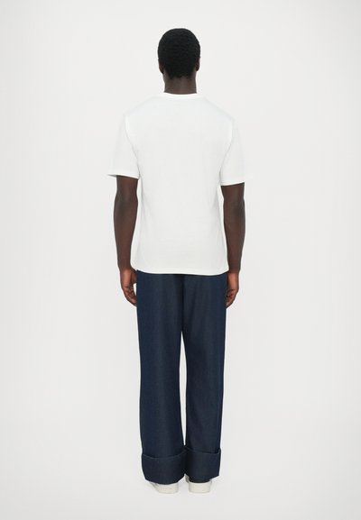 T-shirt blanc en coton associé à un jean large bleu foncé, avec des manches retroussées et des baskets blanches. Tenue simple et décontractée vue de dos.