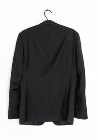 Veste noire en tissu texturé avec fente unique et revers crantés. Comprend deux poches latérales et une boucle de suspension.