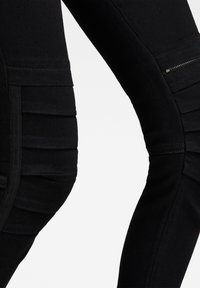 Leggings de mezclilla negra con textura acanalada y un detalle de bolsillo con cremallera en el lado, que se estrechan hacia el tobillo. Acabado suave en toda la prenda.