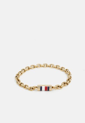Bracelet en chaîne dorée avec un fermoir cylindrique arborant des rayures rouge, blanche et bleue sur un fond blanc.