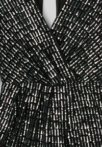 Robe noire avec un décolleté en V profond, recouverte de rangées verticales de sequins argentés scintillants, avec un détail de taille plissée.