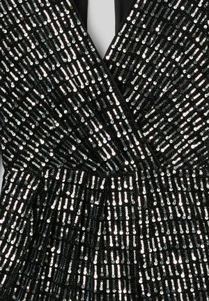 Robe noire avec un décolleté en V profond, recouverte de rangées verticales de sequins argentés scintillants, avec un détail de taille plissée.