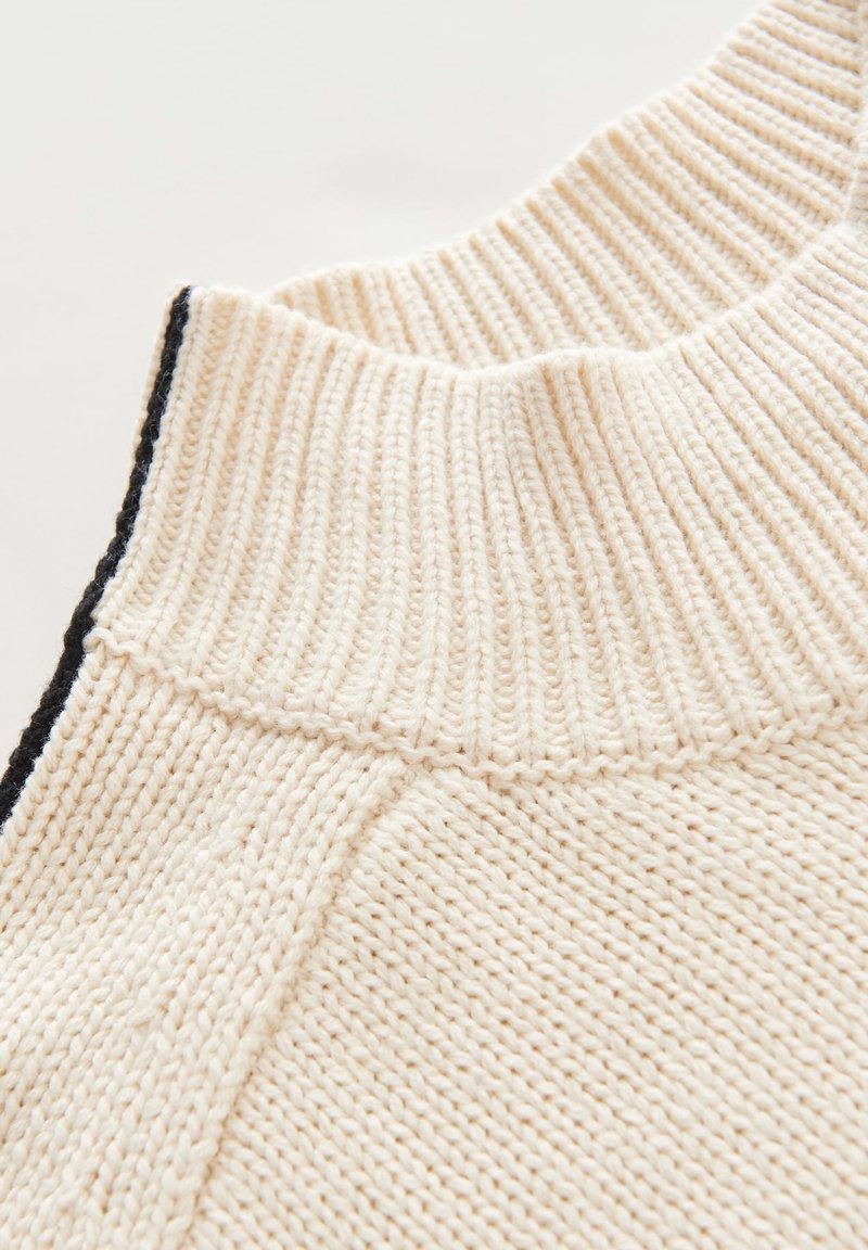 Strickpullover mit einem gerippten, cremefarbenen Kragen und schwarzen Akzenten. Verfügt über einen strukturierten Stoff mit sichtbaren Nähten und einem nahtlosen Design.