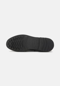 Suela de zapato negra con agarre texturizado, que presenta un patrón de estrellas y líneas. Se aprecian bordes lisos y una construcción robusta.