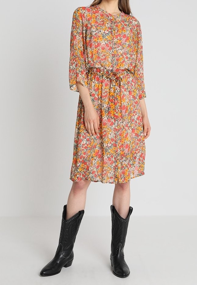 Blommig klänning med ett flerfärgat mönster i rosa, orange och grönt, med lös passform, trekvartsärmar och dragsko i midjan. Bärs med svarta cowboystövlar.