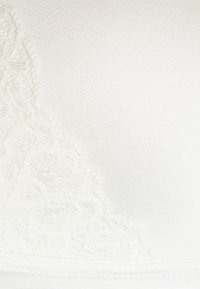 Senza cuciture in pizzo bianco, caratterizzata da un tessuto liscio e testurizzato con dettagli in pizzo floreale sul lato sinistro e un semplice elastico.