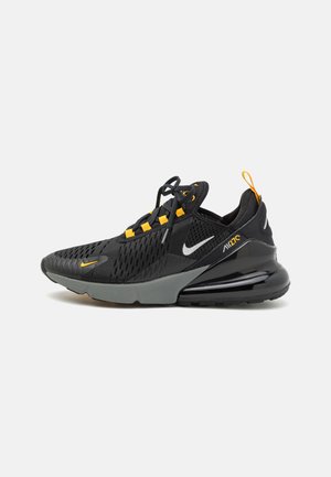 Scarpa da ginnastica nera con tomaia in rete, suola grigia e accenti arancioni. Presenta un logo, lacci e un tallone imbottito per il supporto.