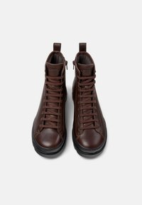 Brązowe skórzane buty typu high-top z pasującymi sznurówkami, gumowymi podeszwami i bocznymi zamkami, charakteryzujące się minimalistycznym designem i markowymi akcentami.