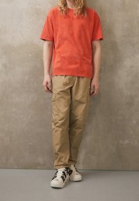 Kortärmad t-shirt i rostfärg med avslappnad passform, i kombination med beiga cargobyxor med fickor och vita sneakers med svarta detaljer.