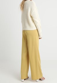 Chunky stickad krämfärgad tröja med avslappnad passform, tillsammans med vida byxor i senapsgul. Modellen bär ljusa klackar.