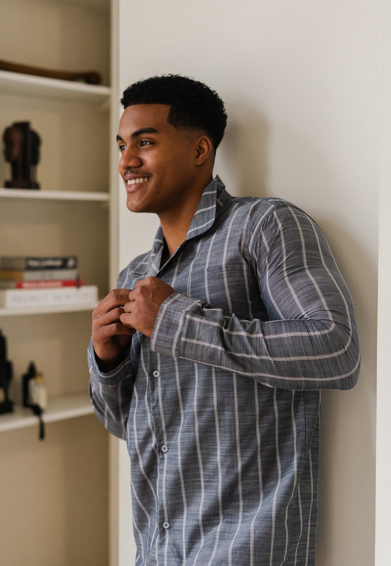 Blauw en wit gestreepte lange mouwen overhemd met kraag, textuurstof en klassieke pasvorm, wordt aangepast door een persoon.