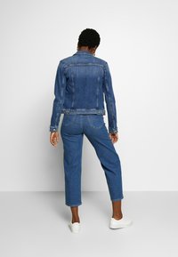 Jeansjacka med långa ärmar, en figurnära design och en medelblå tvätt. Tillsammans med vida jeans och vita sneakers.