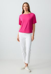 Top fucsia a maniche corte con scollo a barca, abbinato a jeans bianchi a gamba dritta e sneakers bianche su uno sfondo chiaro.