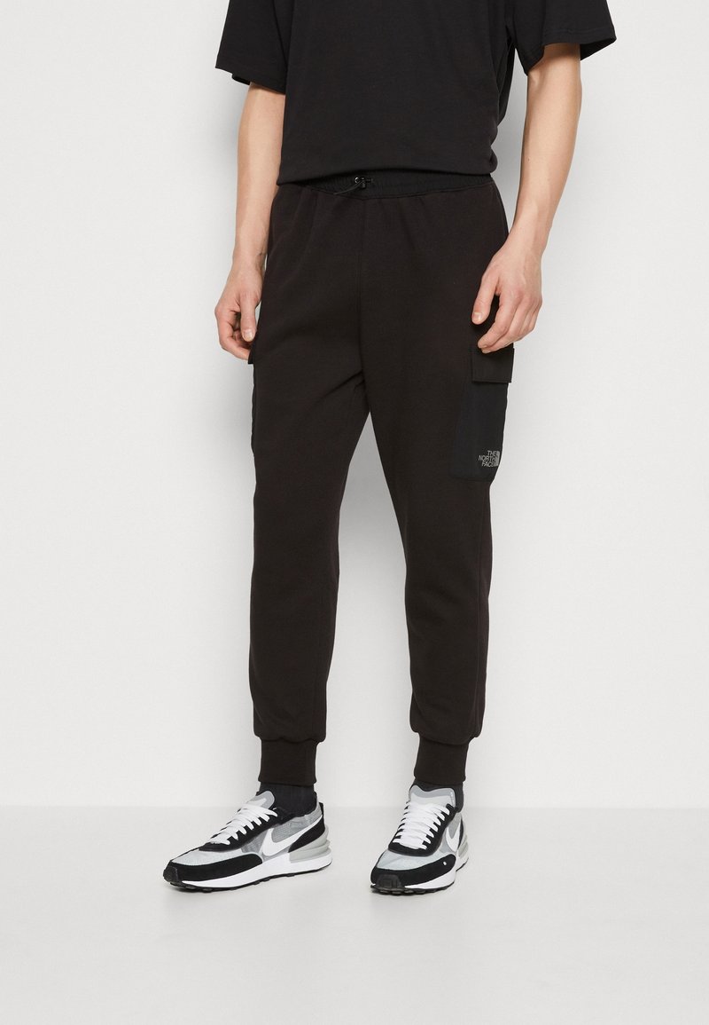 Pantalones de chándal negros hechos de tela suave, con una cintura elástica, puños ajustados y un bolsillo de carga lateral con detalle de logo.