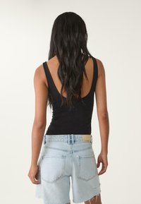 Svart ärmlös bodysuit med låg rygg, tillsammans med ljusblå denimshorts med fransad fåll och bakfickor.