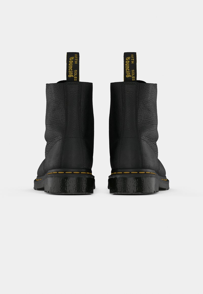 Un par de botas de cuero negro hasta el tobillo con costuras amarillas y tiras de agarre que dicen "CON SUELAS REBOTANTES", mostradas desde la parte trasera sobre un fondo blanco.