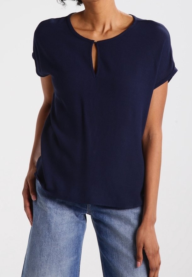 Top blu navy a maniche corte realizzato in tessuto morbido, con dettaglio a chiave sul collo e una vestibilità rilassata. Abbinato a jeans chiari.