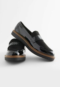 Mocassini in pelle verniciata nera con dettagli in suede e accenti traforati; suola piatta con un leggero bordo marrone; design elegante e arrotondato.
