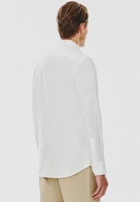 Biała koszula z długim rękawem, klasycznym kołnierzykiem, zapinanymi mankietami i zaokrąglonym dołem. Posiada gładką teksturę i lekką tkaninę.