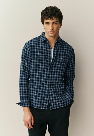 Marineblau kariertes Hemd mit langen Ärmeln, durchgehend mit Knöpfen und zwei Brusttaschen. Verfügt über eine gewebte Textur und ein kontrastierendes weißes Gittermuster.