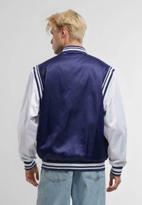 Navy satin varsity jacket with white sleeves, striped cuffs, and collar. Features a smooth texture and athletic design. Back view.