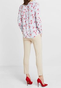 Blus med blommönster i blått och vitt, kombinerad med beigefärgade tapered-byxor och röda högklackade skor.