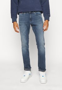 Tmavě modré jeansy slim fit, s vybledlým umytím, designem s pěti kapsami a jemnými švy, v kombinaci s bílými teniskami.