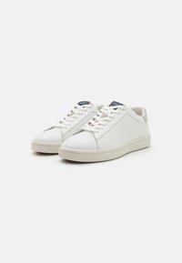 Vita lädersneakers med en slät yta, rund tå och snörningsdesign. Har en kontrasterande ljus hälflik och logofärger.