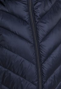 Granatowa kurtka puchowa z przeszyciami w kształcie jodełki, wyposażona w srebrny zamek błyskawiczny oraz gładką, błyszczącą fakturę tkaniny. Lekka i ocieplana.