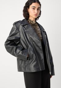 Černá bunda z umělé kůže ve stylu biker s texturovaným povrchem, asymetrickým zapínáním na zip a kapsami na zip; spárovaná s topem s leopardím vzorem.