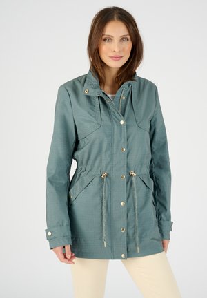 Veste légère en bleu sarcelle avec fermeture éclair et pression, taille cintrée, grandes poches avant et capuche, présentant un motif texturé subtil.