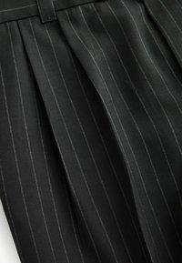 Black pinstriped fabric with a herringbone pattern, featuring crisp pleats and a smooth texture. Stitching in a contrasting color is visible.
