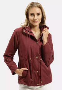 Bordowa, lekka kurtka z wysokim kołnierzem, elastycznym paskiem w talii, dwoma przednimi kieszeniami i złotymi napami. Gładka tekstura, casualowy krój.