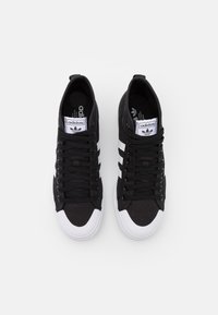 Svarta canvas sneakers med vit gummitå, tre vita ränder på sidorna och svarta snören. Har en Adidas-logga på tungan.