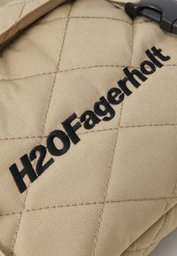 Kilimėlių beigi audinys su juodu išsiuvinėtu tekstu "H2OFagerholt." Pasižymi tekstūruota paviršiumi ir įstrižais siuvimo raštais.