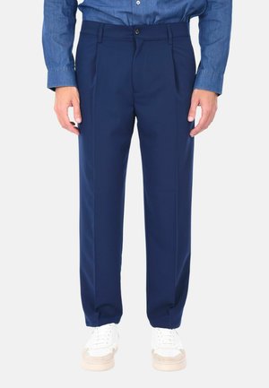 Pantaloni tailored blu navy realizzati in un tessuto liscio, con una vestibilità rilassata, pieghe singole e tasche laterali, abbinati a sneakers bianche.