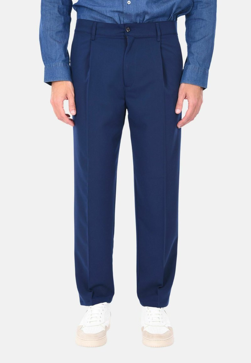 Pantaloni tailored blu navy realizzati in un tessuto liscio, con una vestibilità rilassata, pieghe singole e tasche laterali, abbinati a sneakers bianche.