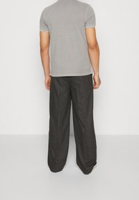 Grå kortärmad t-shirt och vida svarta byxor med pinstrimma. Byxorna har ett strukturerat tyg med synliga sömdetaljer och en lös passform.