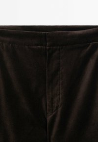 Gros plan sur la ceinture et le devant supérieur d'un pantalon marron foncé avec une fermeture éclair cachée à l'avant et une texture de tissu lisse.