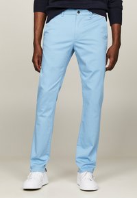 Jasnoniebieskie chinosy wykonane z bawełnianej tkaniny, z płaskim przodem, dwoma bocznymi kieszeniami i pojedynczym zapięciem na guzik. Połączone z białymi trampkami.