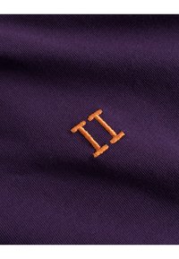 Fialová tkanina s texturovaným povrchem, na které je vyšívané "II" jasně oranžovou nití.