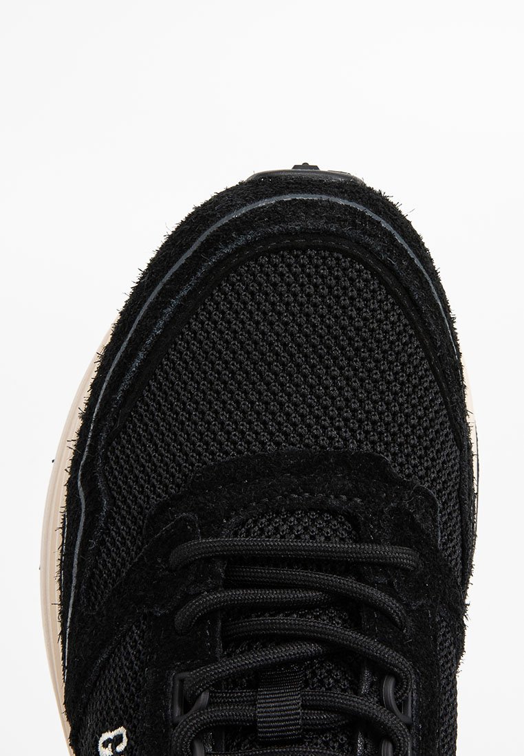 Baskets de sport noires avec une tige en mesh, lacets noirs et semelle beige vues de dessus.