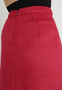 Jupe rouge en tissu doux, avec une coupe slim, taille élastique et fermeture éclair au dos. Texture lisse avec des détails de couture minimaux.